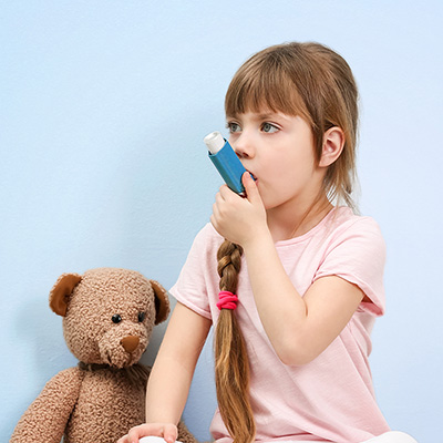 Child Using Asthma Inhaler With Teddy Bear By Her Side
