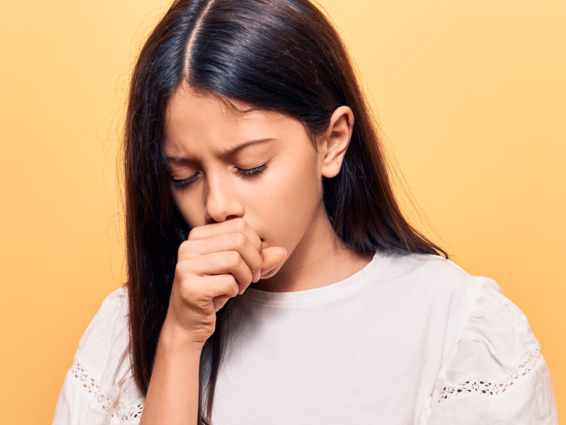 Child coughing - head and shoulders holding hand to her face on a yellow background