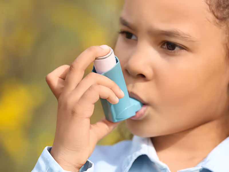 Child With Inhaler In Front Of Greenery