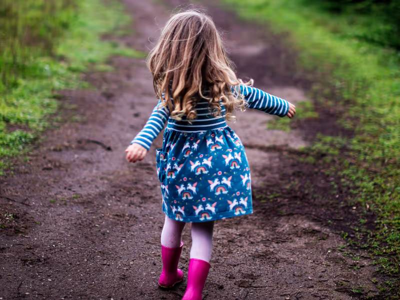 Small Child Walking A Path Wearing Pink Wellies And A Sun Dress